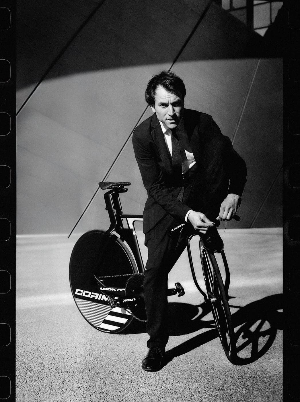 Clément Leroy en costume accroupi derrière un vélo LOOK/CORIMA — bordure pellicule