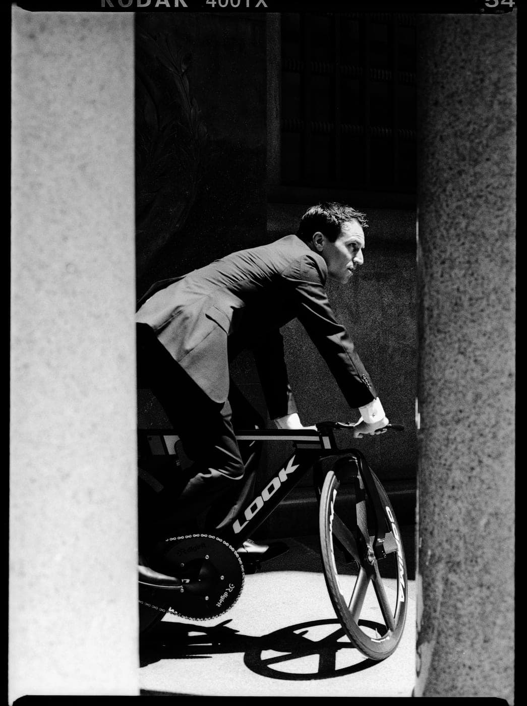 Clément Leroy en costume pédalant entre des piliers de pierre — style Kodak 400TX
